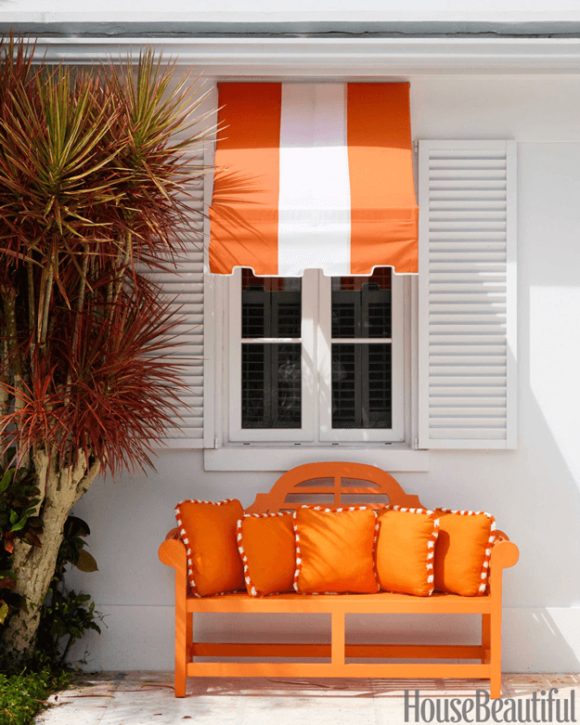 white home exterior with orange bench and striped awning